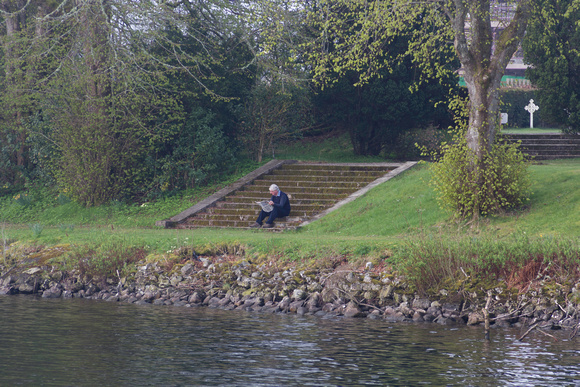 Man sitting on steps reading paper on shore of Loch Ness