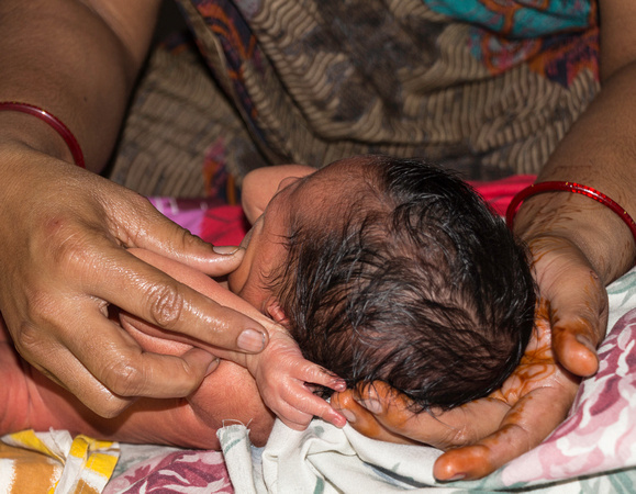 Masseuse doing light massage of hands of a 5 day old Indian baby